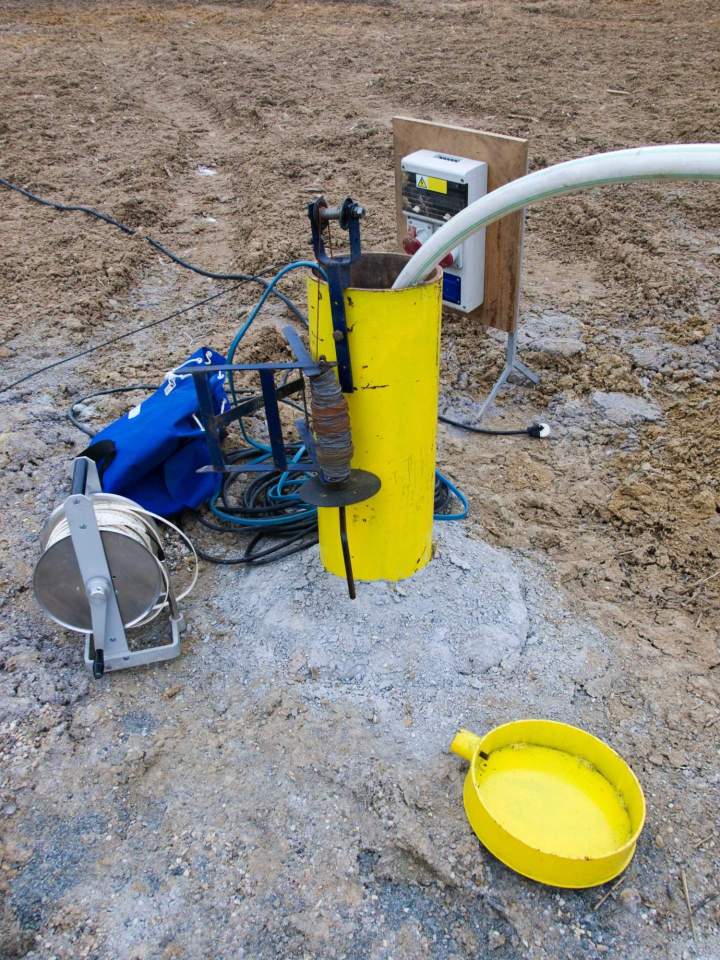Technicien installant un tube de piézomètre dans un forage, avec le matériel de mesure à proximité et un environnement naturel.